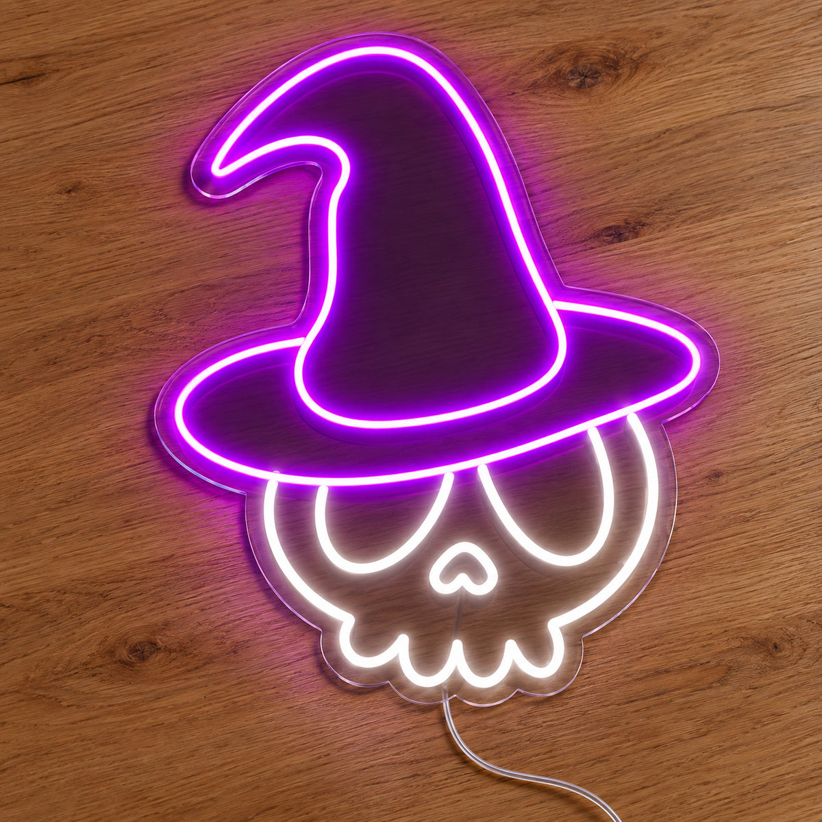 Skull with Witch Hat Neon Sign featuring a white skull wearing a tall purple witch hat, illuminated on clear acrylic lying on a natural oak wooden surface.