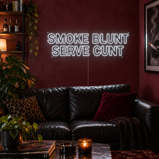 Smoke Blunt Serve Cunt Neon Sign glowing white above a black leather sofa.