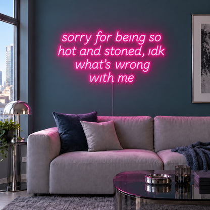 Rose Red version of the Sorry For Being So Hot And Stoned, Idk What's Wrong With Me Neon Sign, shown above a grey sofa against a blue wall.