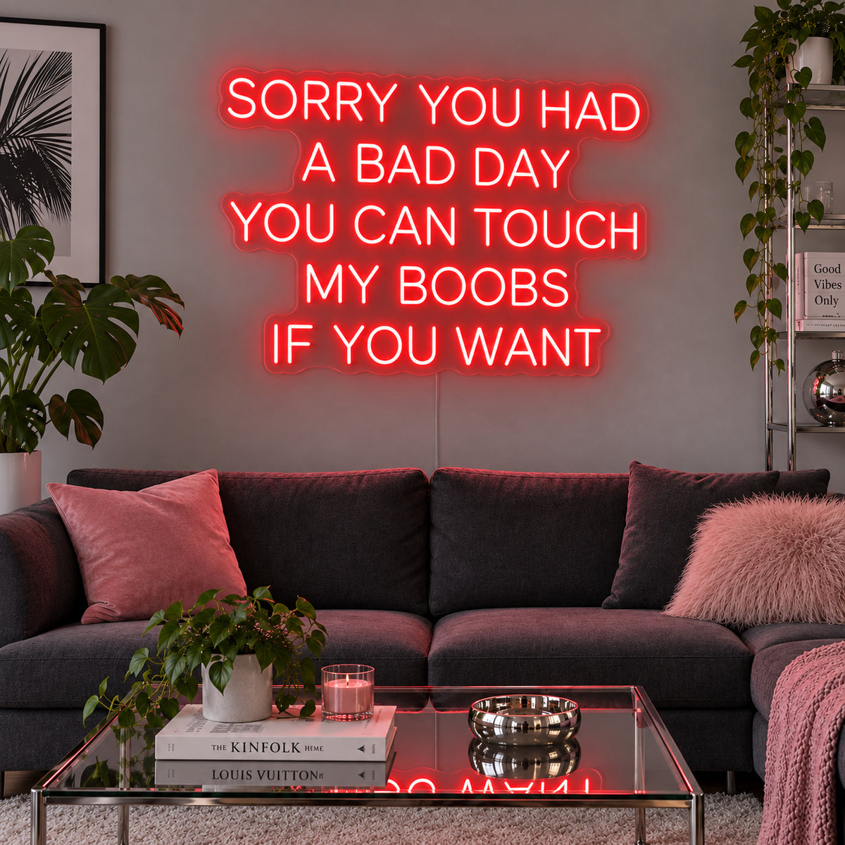 Sorry You Had A Bad Day You Can Touch My Boobs If You Want Neon Sign with red lighting, displayed above a grey sofa with pink cushions.