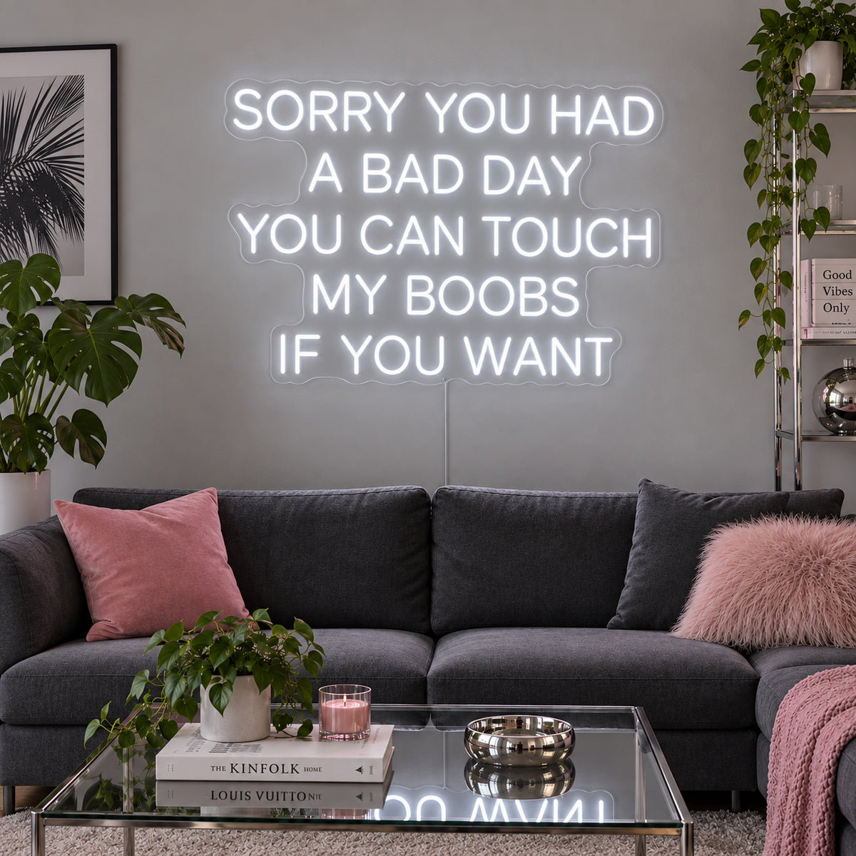 Sorry You Had A Bad Day You Can Touch My Boobs If You Want Neon Sign glowing white above a grey sofa with pink cushions.
