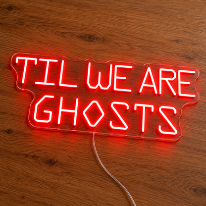 Til We Are Ghosts Block Letter Neon Sign featuring Til We Are Ghosts wording in red geometric block letters, illuminated on clear acrylic lying on a natural oak wooden surface.