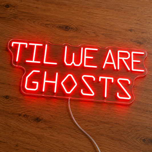 Til We Are Ghosts Block Letter Neon Sign featuring Til We Are Ghosts wording in red geometric block letters, illuminated on clear acrylic lying on a natural oak wooden surface.