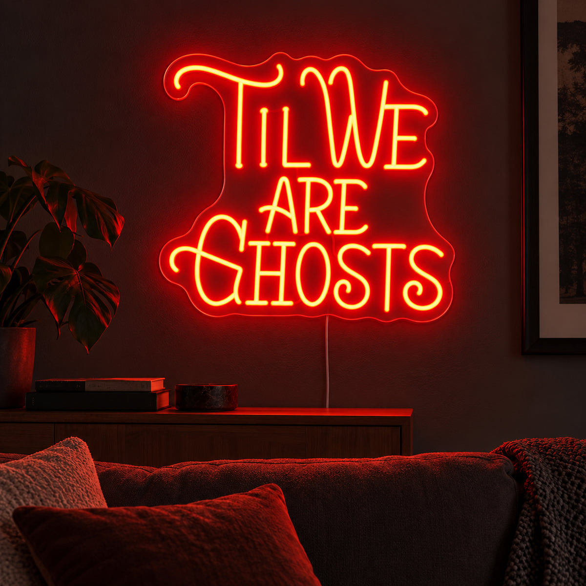 Til We Are Ghosts Ornate Neon Sign featuring Til We Are Ghosts wording in decorative orange lettering with curved flourishes, glowing on a dark living room wall.