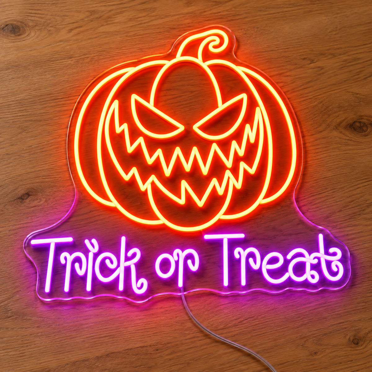 Trick or Treat Pumpkin Neon Sign featuring an orange pumpkin with a jagged grin above purple Trick or Treat lettering, illuminated on clear acrylic lying on a natural oak wooden surface.
