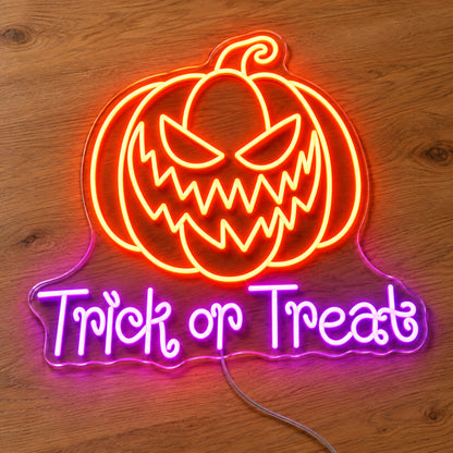 Trick or Treat Pumpkin Neon Sign featuring an orange pumpkin with a jagged grin above purple Trick or Treat lettering, illuminated on clear acrylic lying on a natural oak wooden surface.