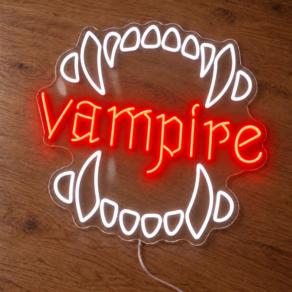 Vampire Fangs Neon Sign featuring white upper and lower fangs surrounding red Vampire lettering, illuminated on clear acrylic lying on a natural oak wooden surface.