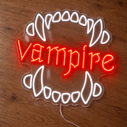 Vampire Fangs Neon Sign featuring white upper and lower fangs surrounding red Vampire lettering, illuminated on clear acrylic lying on a natural oak wooden surface.