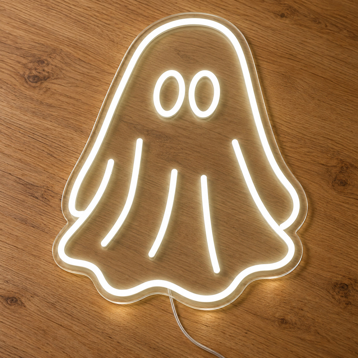 White Ghost Neon Sign featuring a white ghost outline with two oval eyes and a flowing sheet shaped body, illuminated on clear acrylic lying on a natural oak wooden surface.