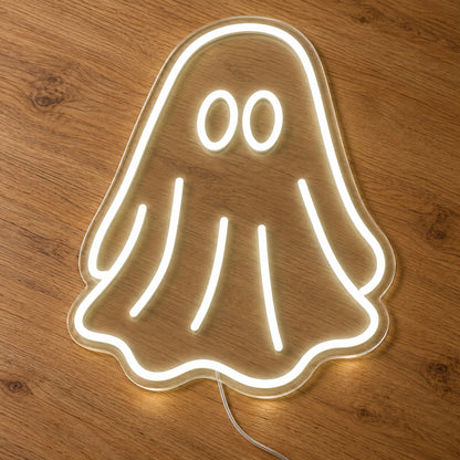 White Ghost Neon Sign featuring a white ghost outline with two oval eyes and a flowing sheet shaped body, illuminated on clear acrylic lying on a natural oak wooden surface.