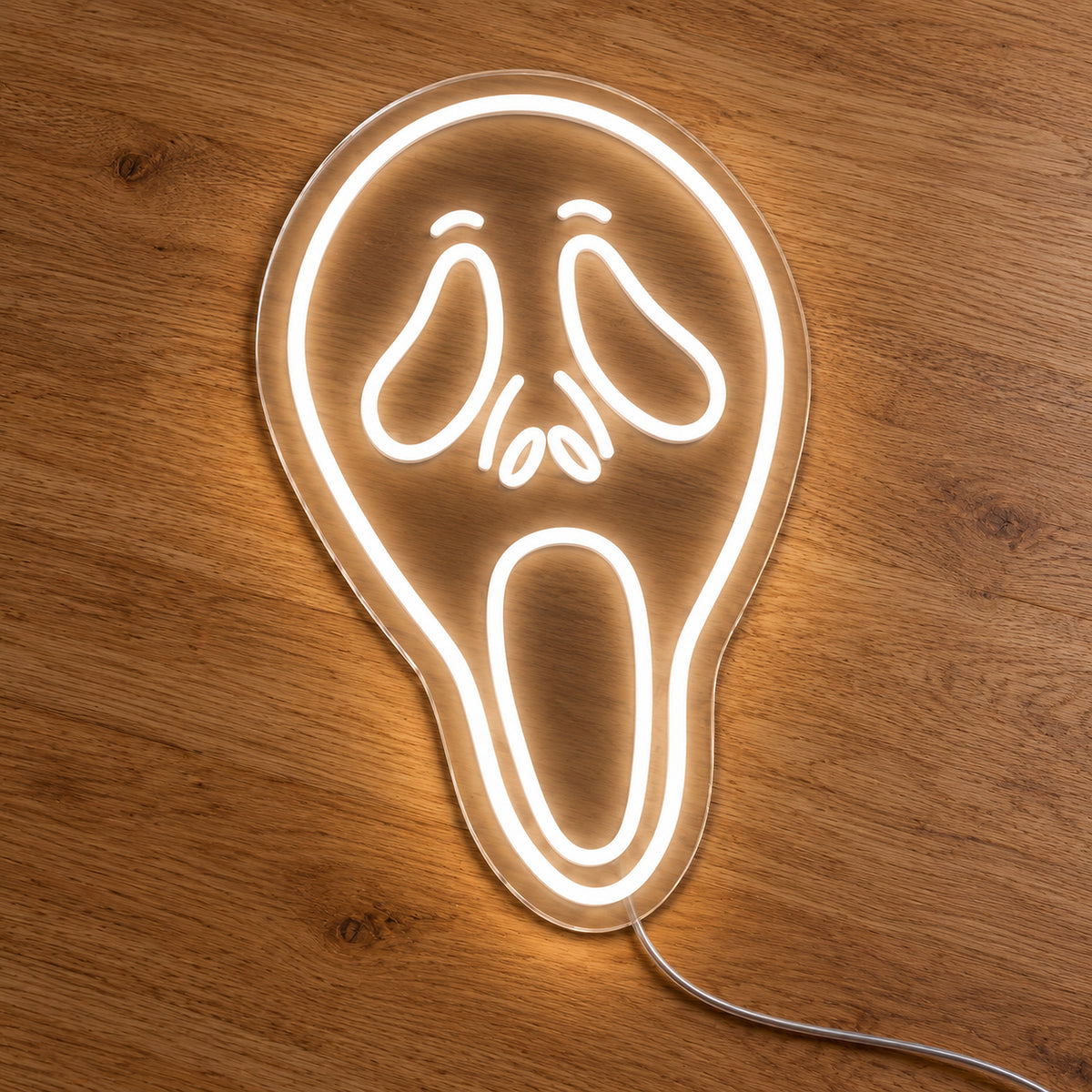White Ghostface Neon Sign featuring the elongated Ghostface mask outlined in white, with drooping eyes and an open mouth, illuminated on clear acrylic lying on a natural oak wooden surface.