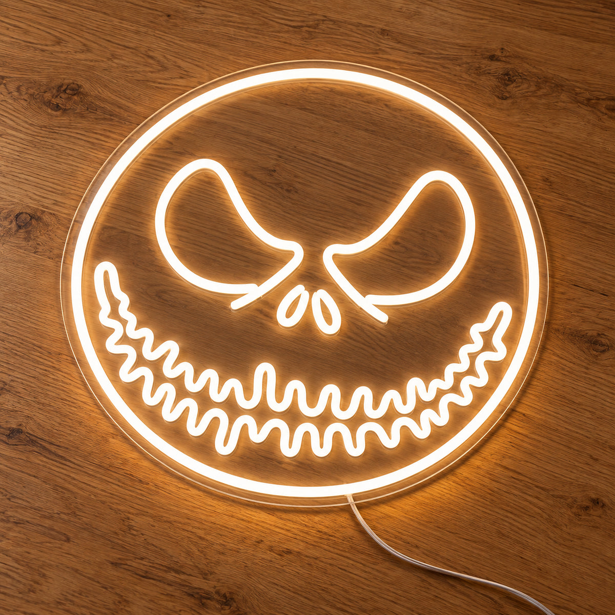 White Jack Skellington Face Neon Sign featuring Jack Skellington's eyes and stitched smile within a white circular face outline, illuminated on clear acrylic lying on a natural oak wooden surface.